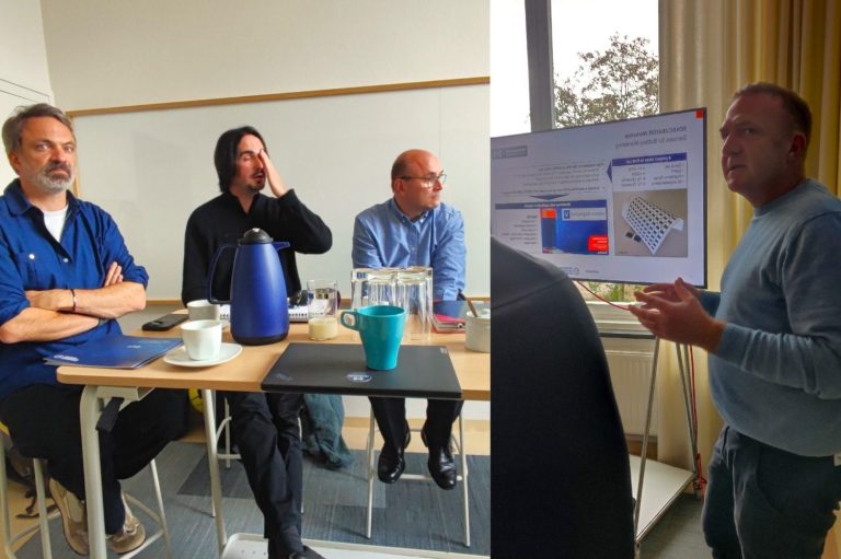 Zwei Gruppen von Männern in einer Besprechung, die an einem Tisch sitzen und präsentieren.