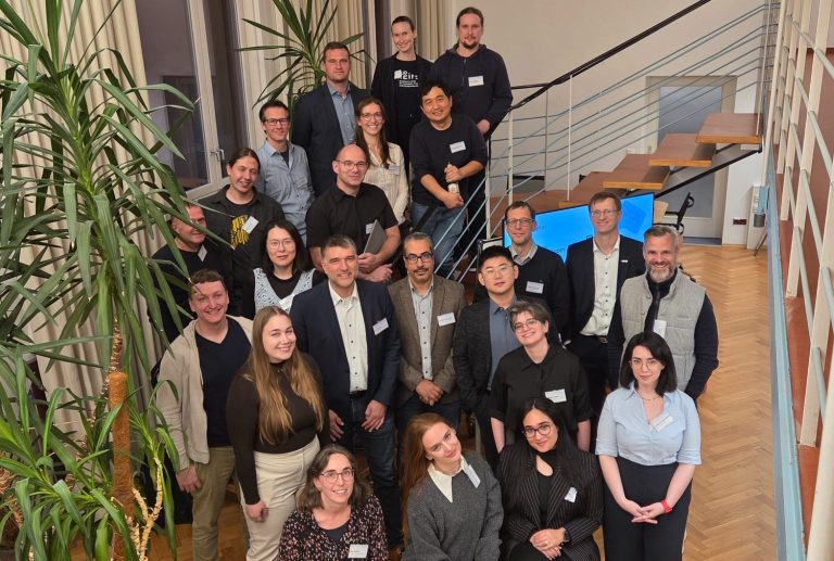 Gruppenfoto von Menschen in einem Innenraum, umgeben von Pflanzen und Treppen.