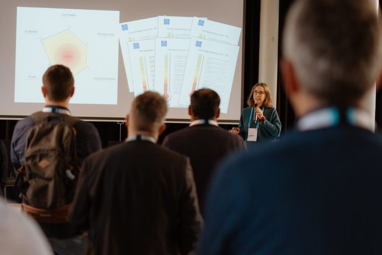 Eine Vortragende präsentiert Grafiken vor einem Publikum in einem Konferenzraum.